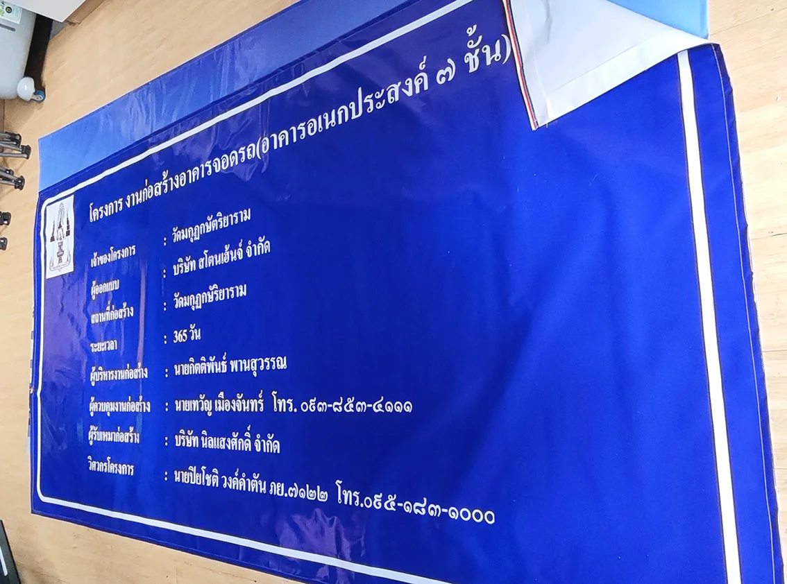 ป้ายโครงการก่อสร้างพื้นหลังสีน้ำเงิน แสดงข้อมูลผู้ว่าจ้าง ผู้รับเหมา เจ้าของงาน และระยะเวลาก่อสร้าง