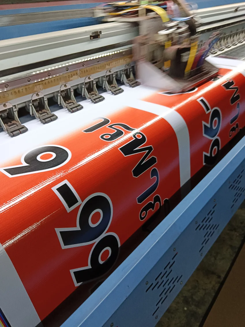 งานพิมพ์ป้ายไวนิลขายอาคารพาณิชย์สีส้มบนเครื่องพิมพ์ขนาดใหญ่ ขณะหัวพิมพ์กำลังทำงาน